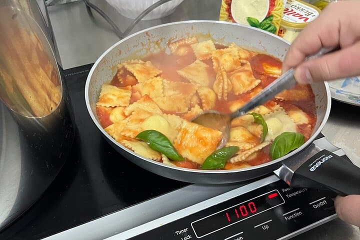 Mixing ravioli with tomato sauce.